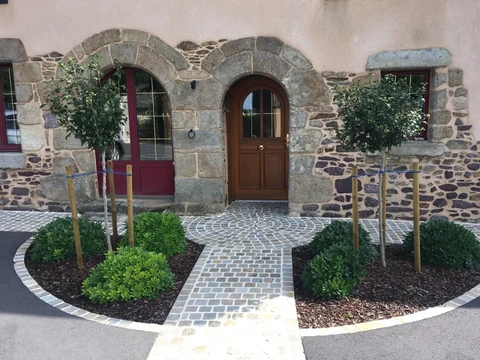Entrée de maison en pierre de granit rénovée, avec une porte cintrée en bois naturel et fenêtres bordeaux