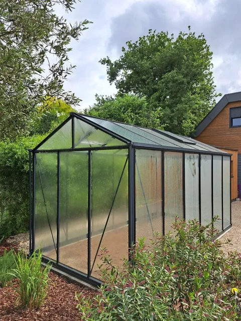 Serre de jardin extérieure, structure aluminium anthracite, vitrage polycarbonate transparent, toit à deux pans avec faîtière, porte coulissante frontale