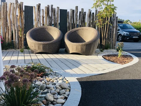 Terrasse extérieure paysagée avec deux fauteuils cocon en résine tressée style rotin, posés sur une dalle bois composite