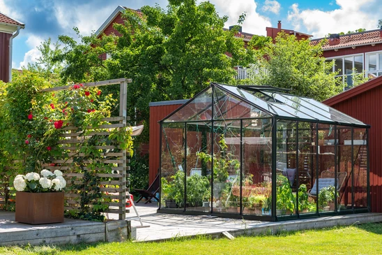 Serre de jardin moderne installée sur terrasse pavée dans espace vert résidentiel
