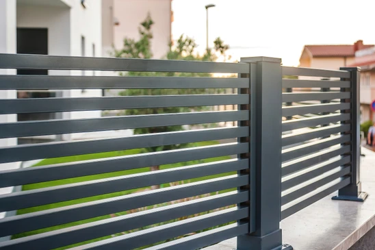 Extérieur résidentiel avec maison moderne blanche, clôture composite anthracite horizontale, pelouse verte entretenue