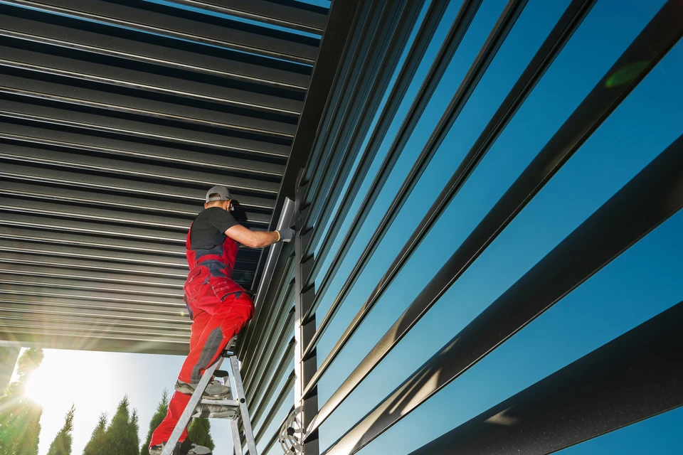 Pergola moderne en acier laqué noir, structure horizontale avec câbles tendus en fil inox, fixée à une façade blanche contemporaine