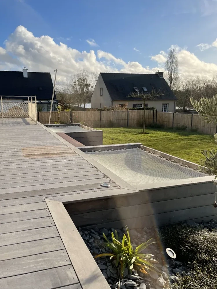 Terrasse extérieure avec mobilier de jardin en métal vert sauge, incluant fauteuils à lattes, table basse ronde en métal et pouf gris