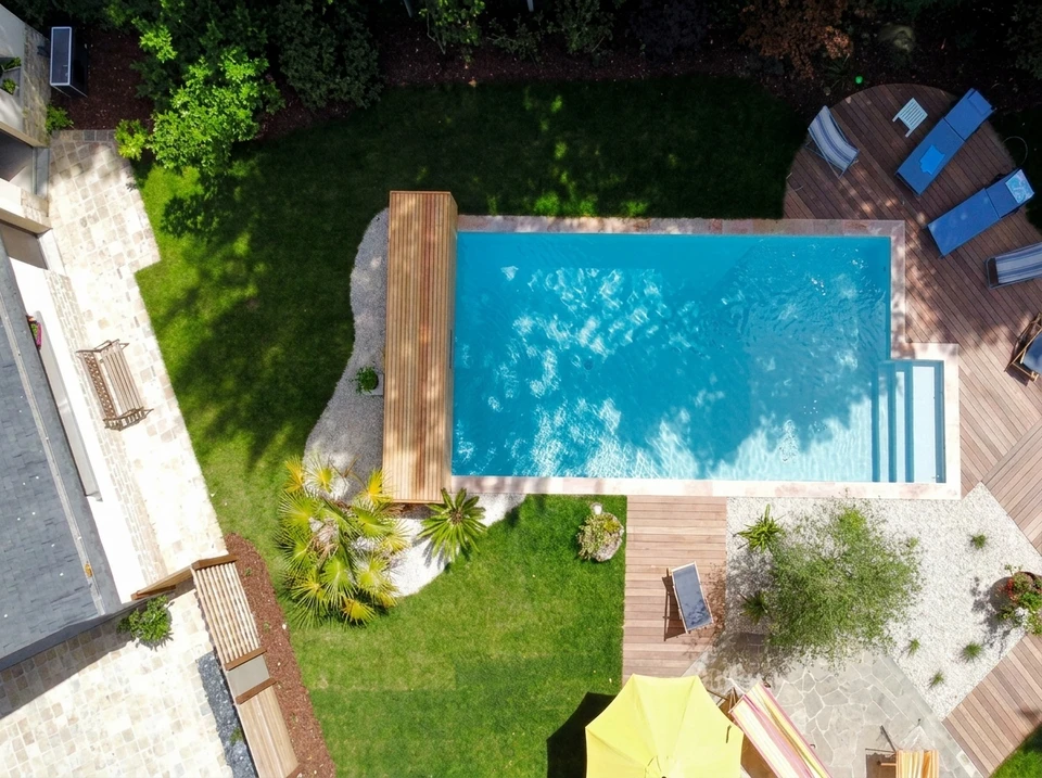 Vue aérienne d'une piscine rectangulaire couloir de nage, revêtement liner bleu, margelles en bois composite IPE, dallage en carrelage grand format grès cérame