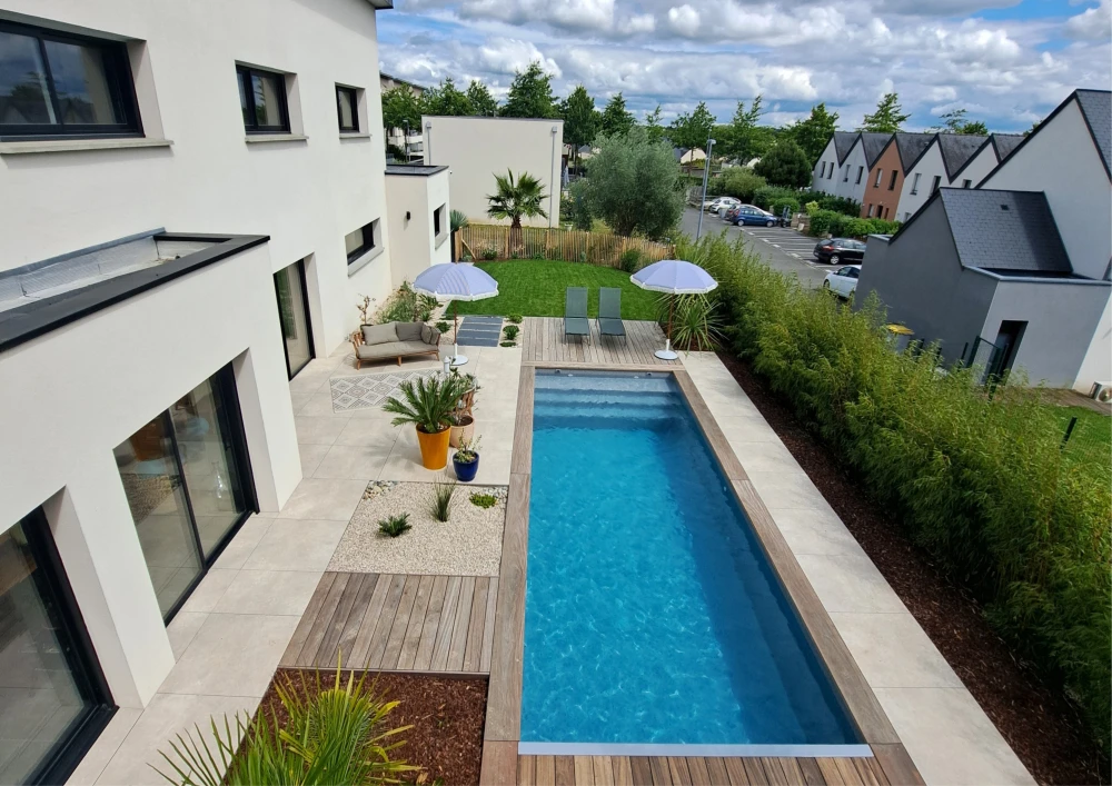 Piscine extérieure à débordement avec margelles en pierre naturelle anthracite, intégrée dans un jardin contemporain